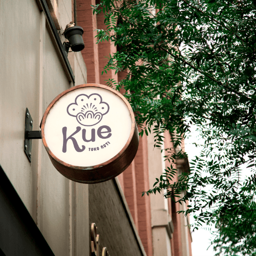 Round Kue bakery sign hanging from a brick storefront