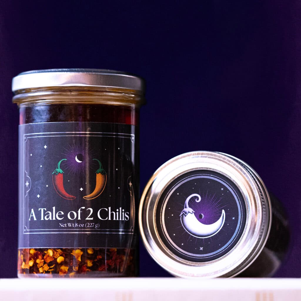 A jar of A Tale of 2 Chilis chili oil next to an open tin, both with the dark purple label